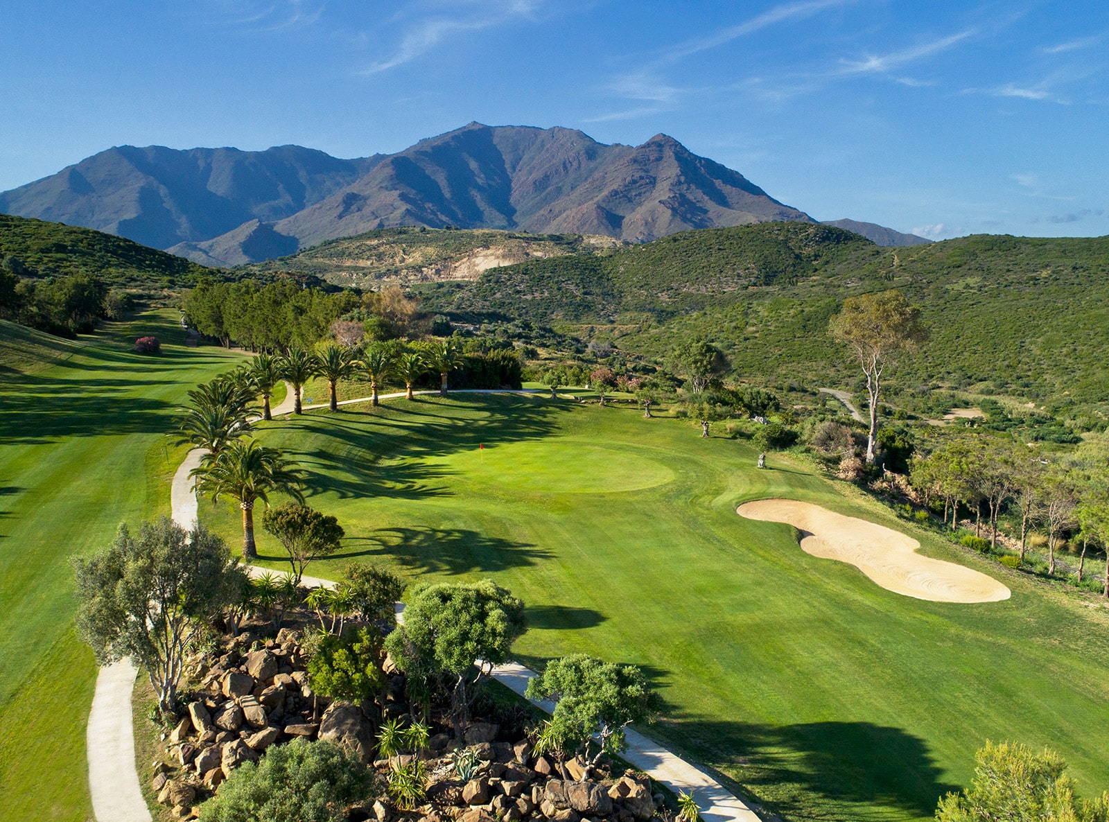 Golfbaan in Estepona met groene fairways en bergen op de achtergrond.