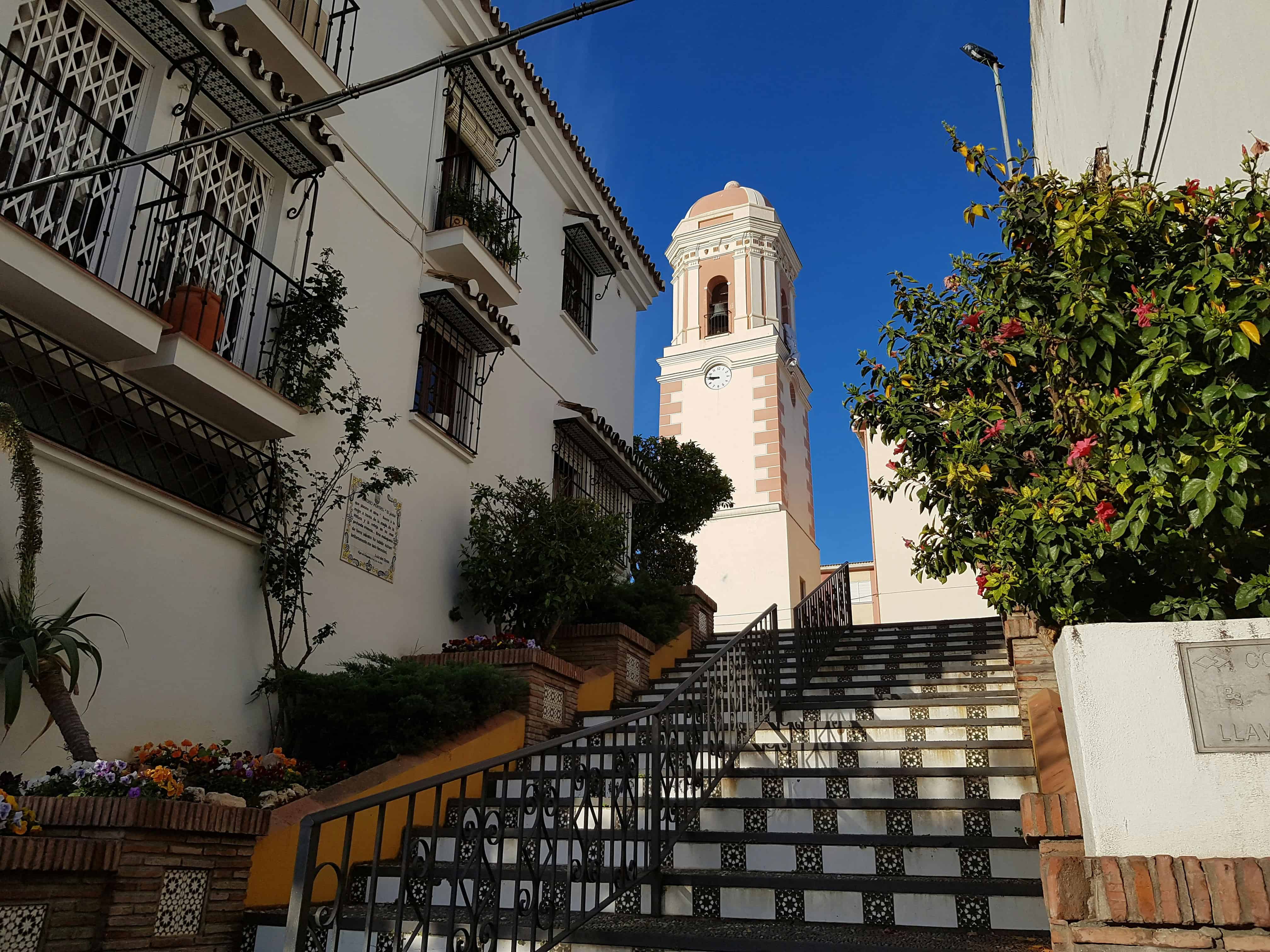 Kerk in Estepona met trap en kleurrijke bloemen, zonnige dag.